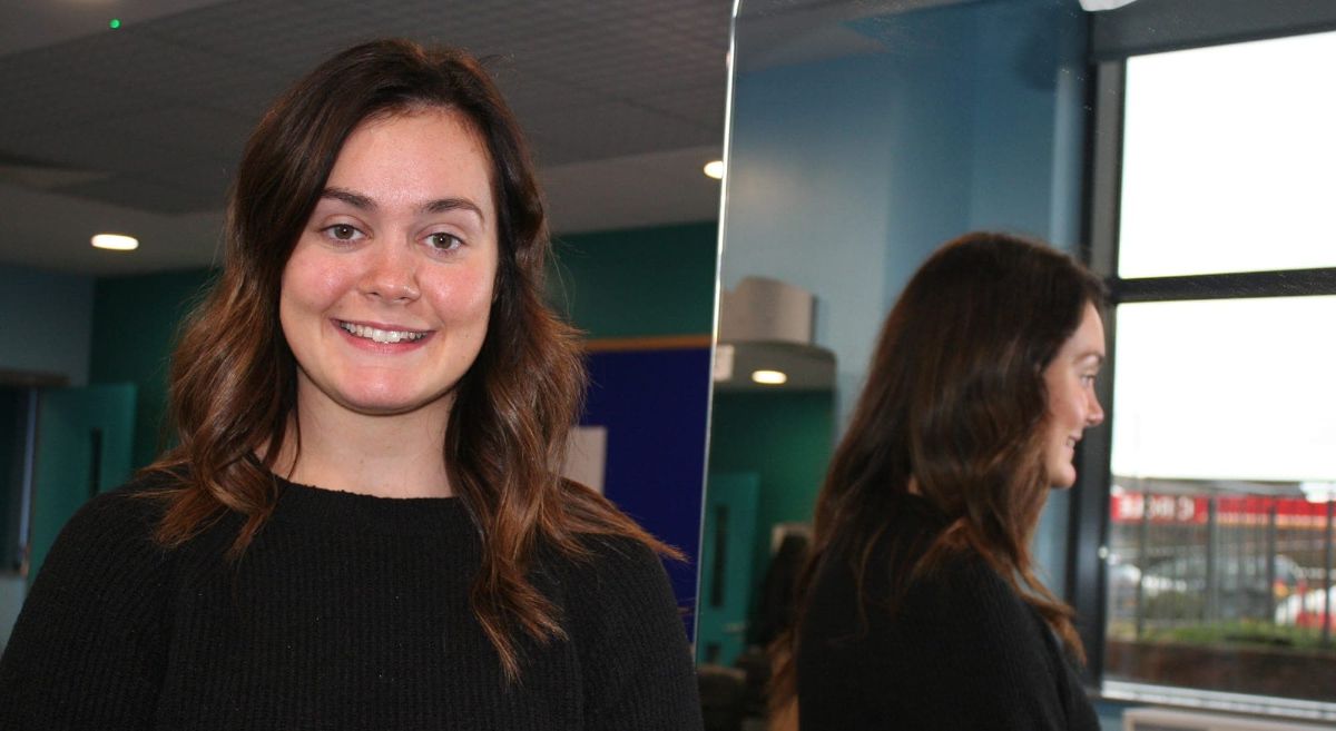 Female with dark long hair smiling to camera with reflection in mirror